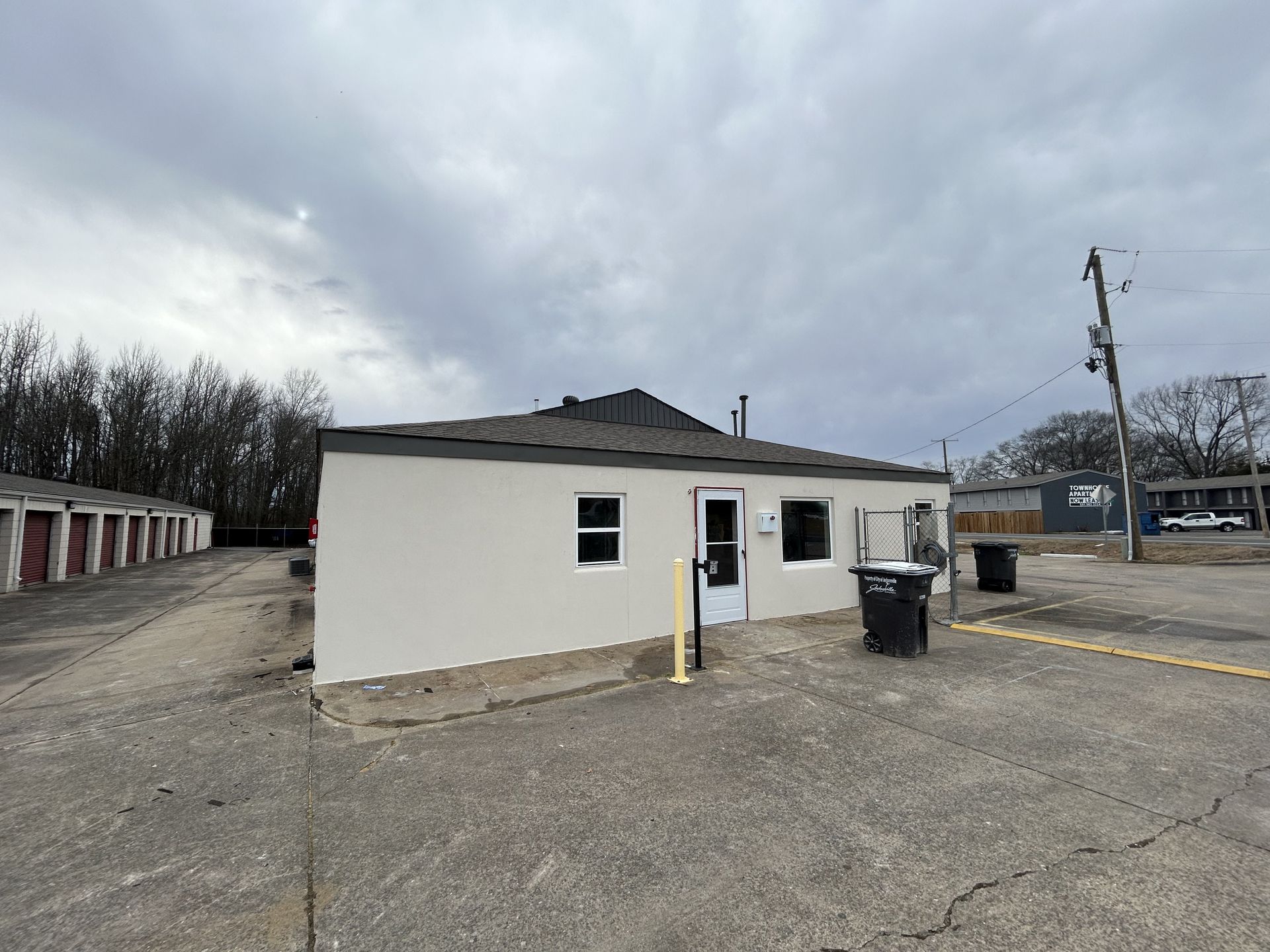 A small white building is sitting in the middle of a parking lot.