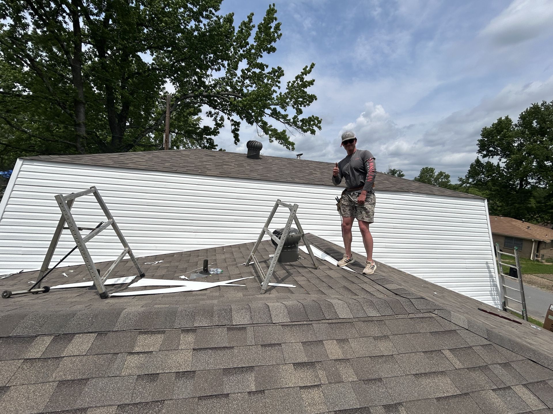 A man is standing on top of a roof with a ladder.