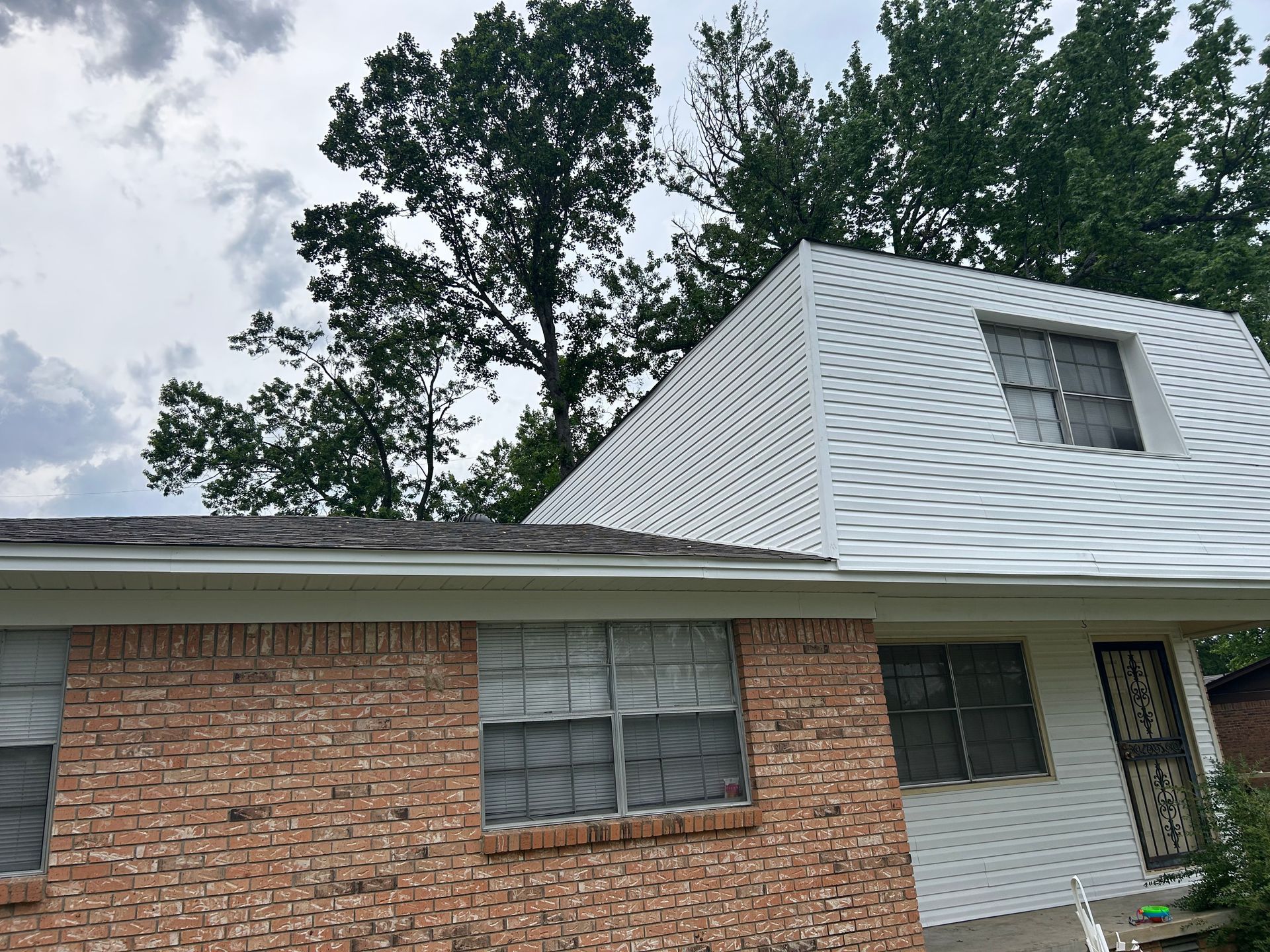 A brick house with a white roof and trees in the background