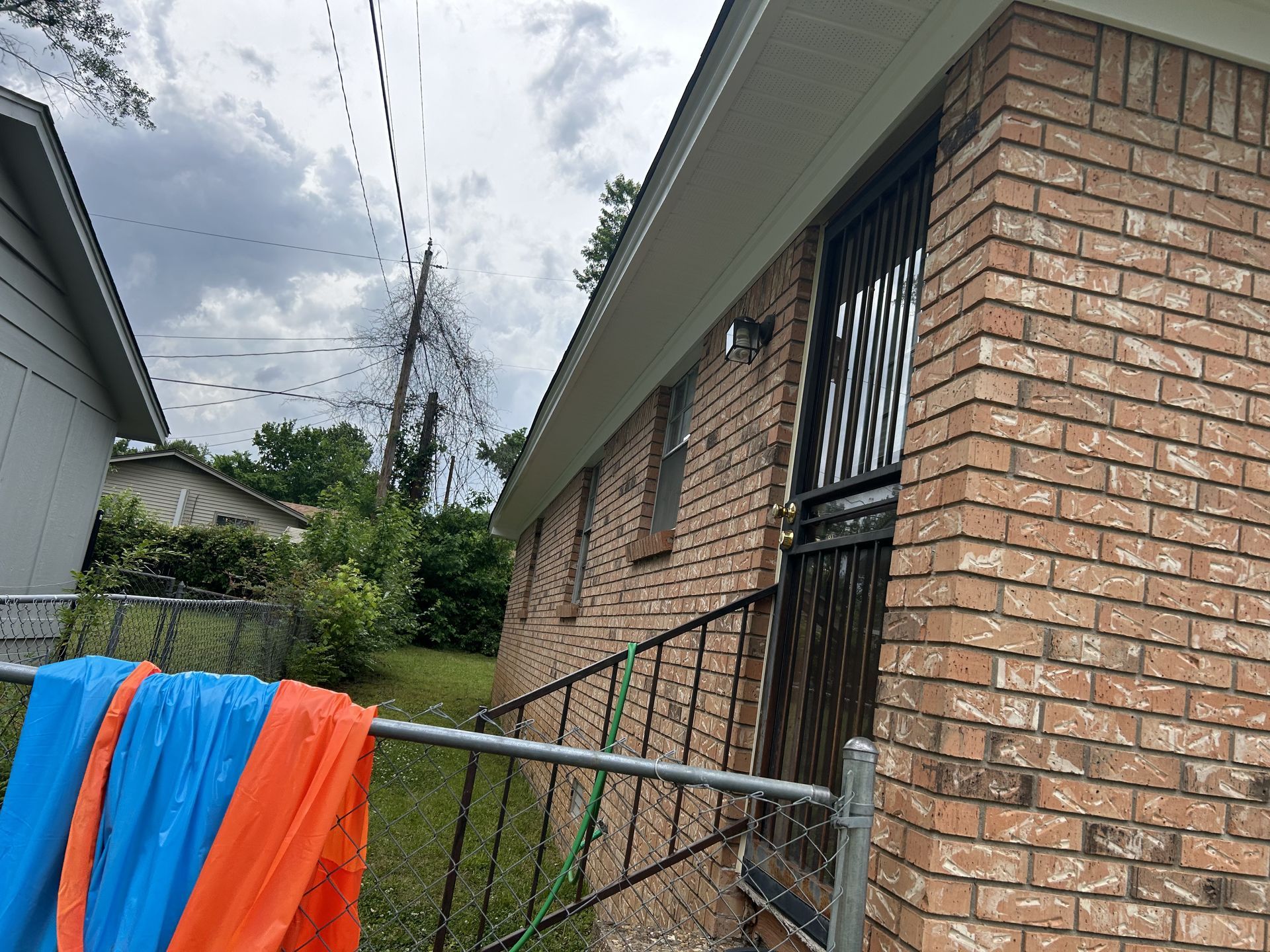 A blue and orange blanket is hanging on a fence in front of a brick building.