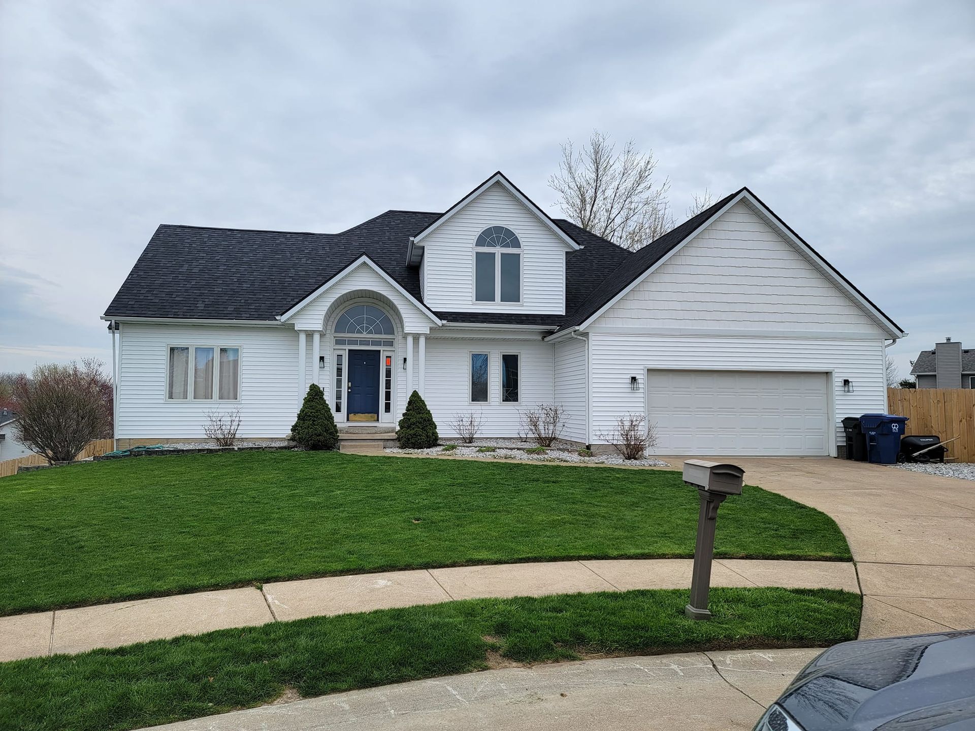 A white house with a black roof and a car parked in front of it.