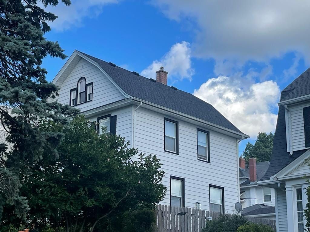 A white house with a black roof is surrounded by trees