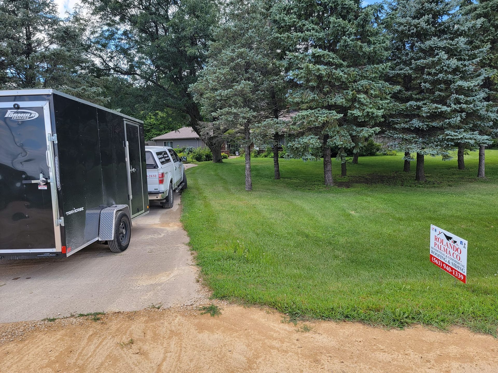 A black trailer is parked on the side of the road next to a for sale sign.
