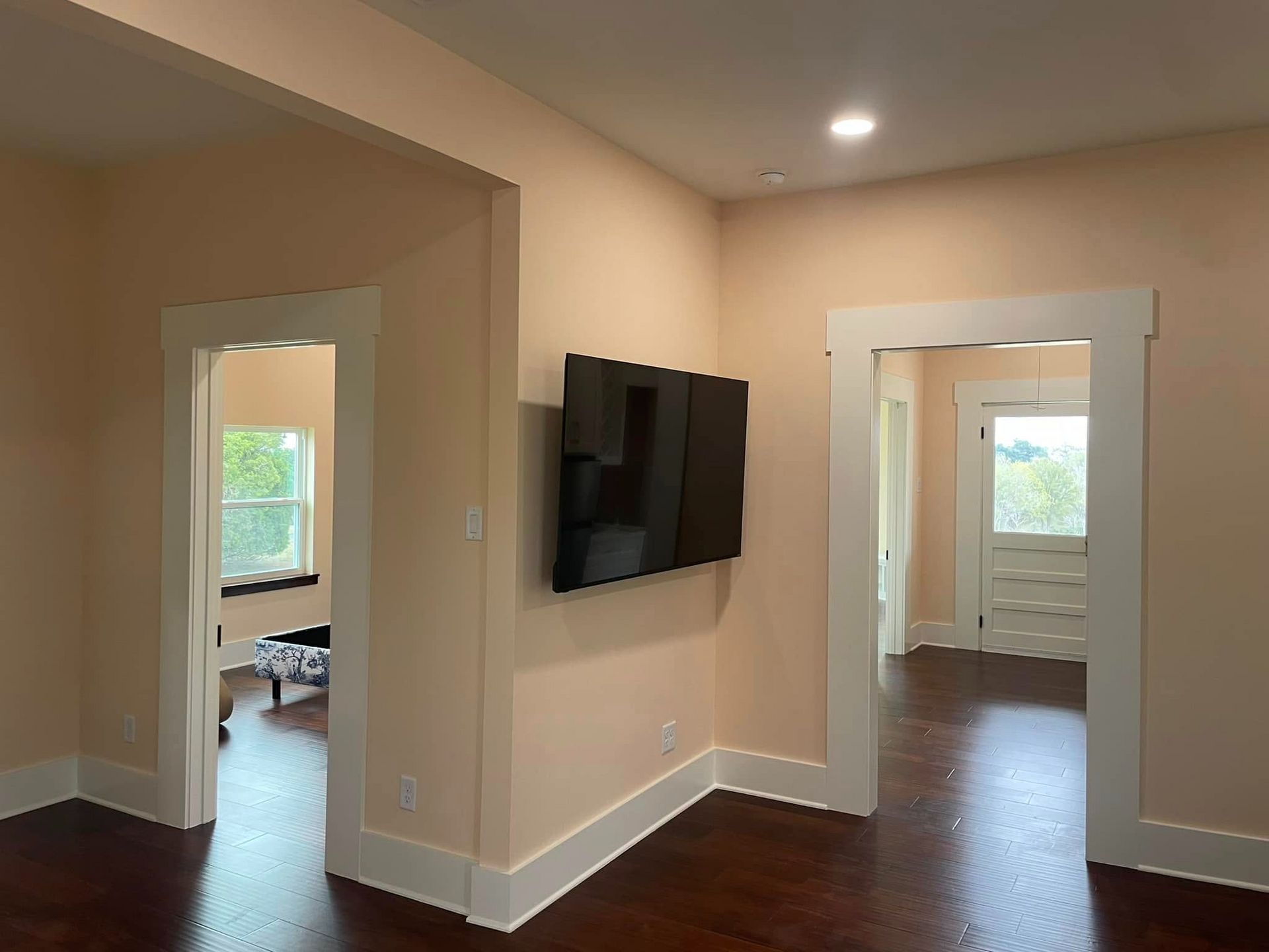 Interior view of a living space with light peach-colored walls and dark wood floors. A TV is mounted on the wall.