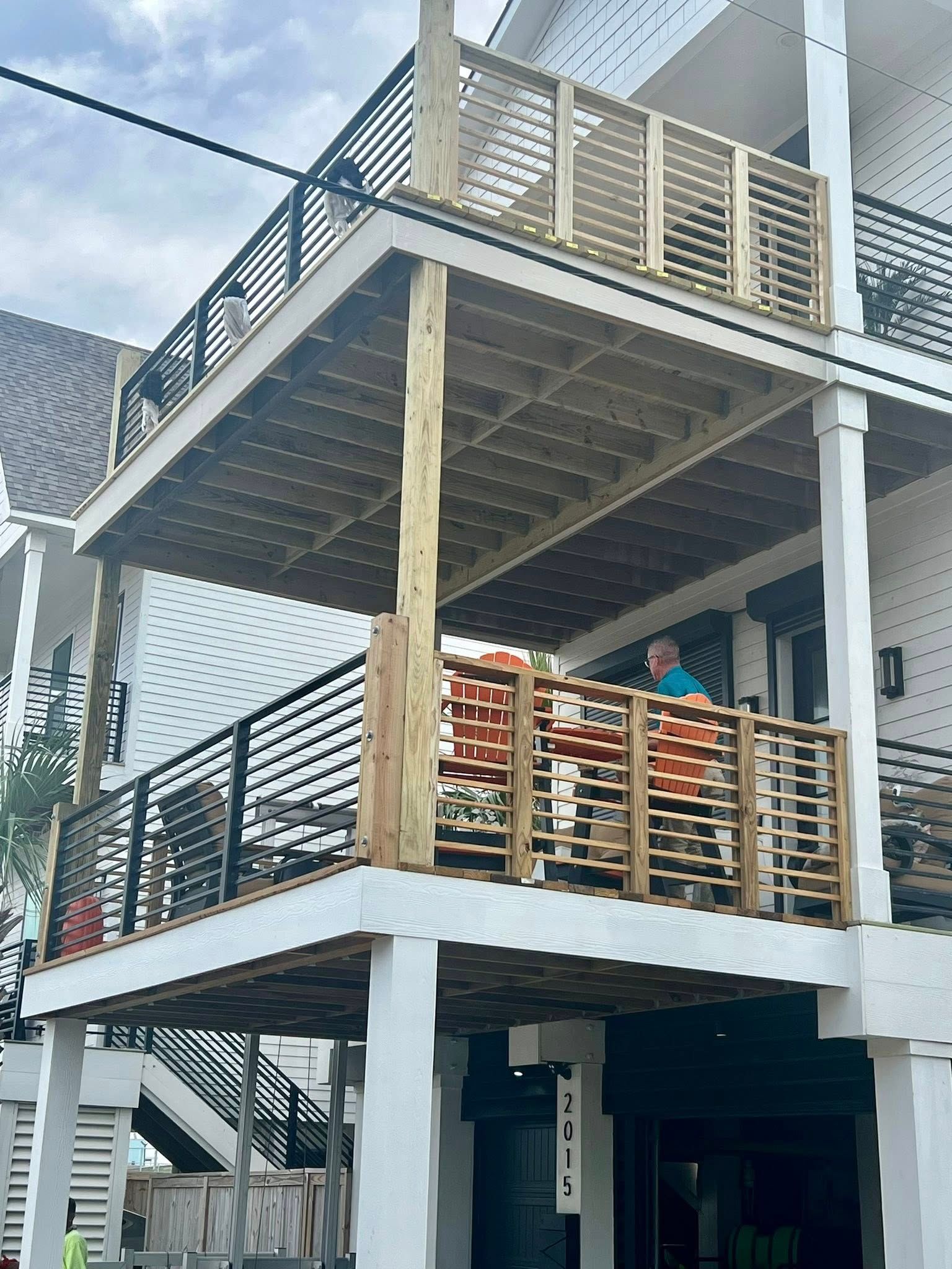 Multi-level wooden deck with black metal railings. A person sits on the lower deck with orange cushions.
