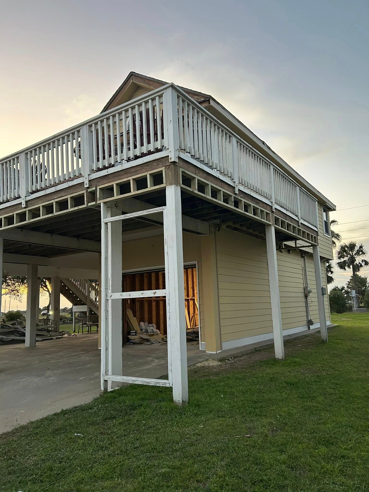 A raised, two-story building with a white deck. Beige siding is visible on the lower level with a glimpse of the interior.