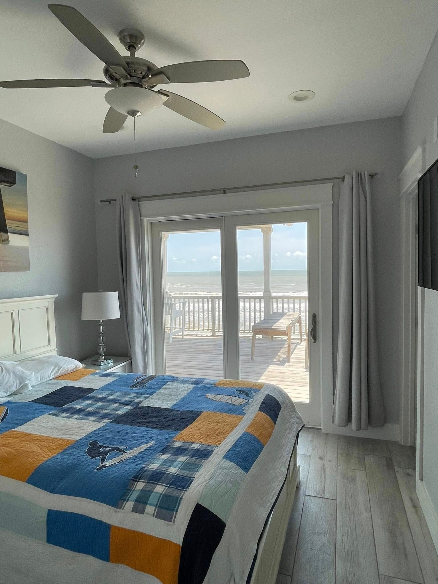 Bedroom with a quilt, balcony overlooking the ocean, and ceiling fan. Soft colors and natural light create a relaxing atmosphere.