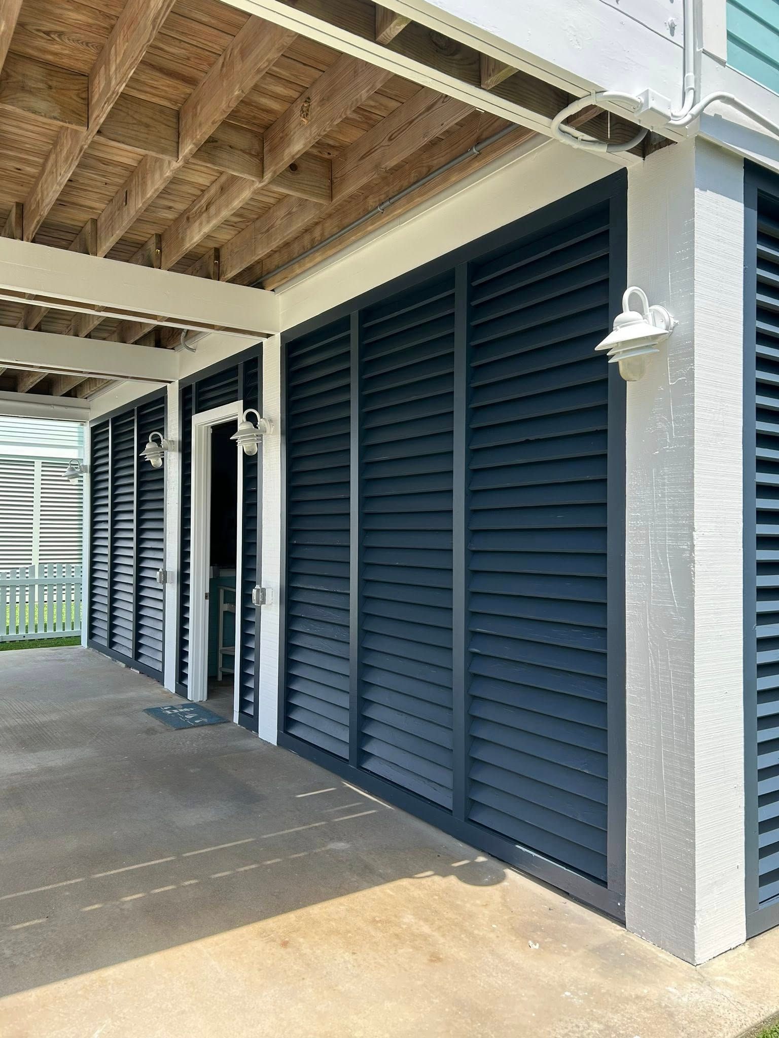 Exterior of a building with navy blue shutters, white trim, and a light brown concrete floor.
