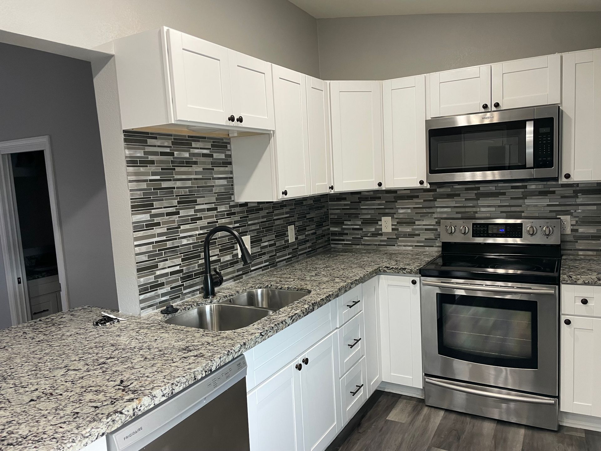 White kitchen with granite countertops, stainless steel appliances, and a mosaic tile backsplash.