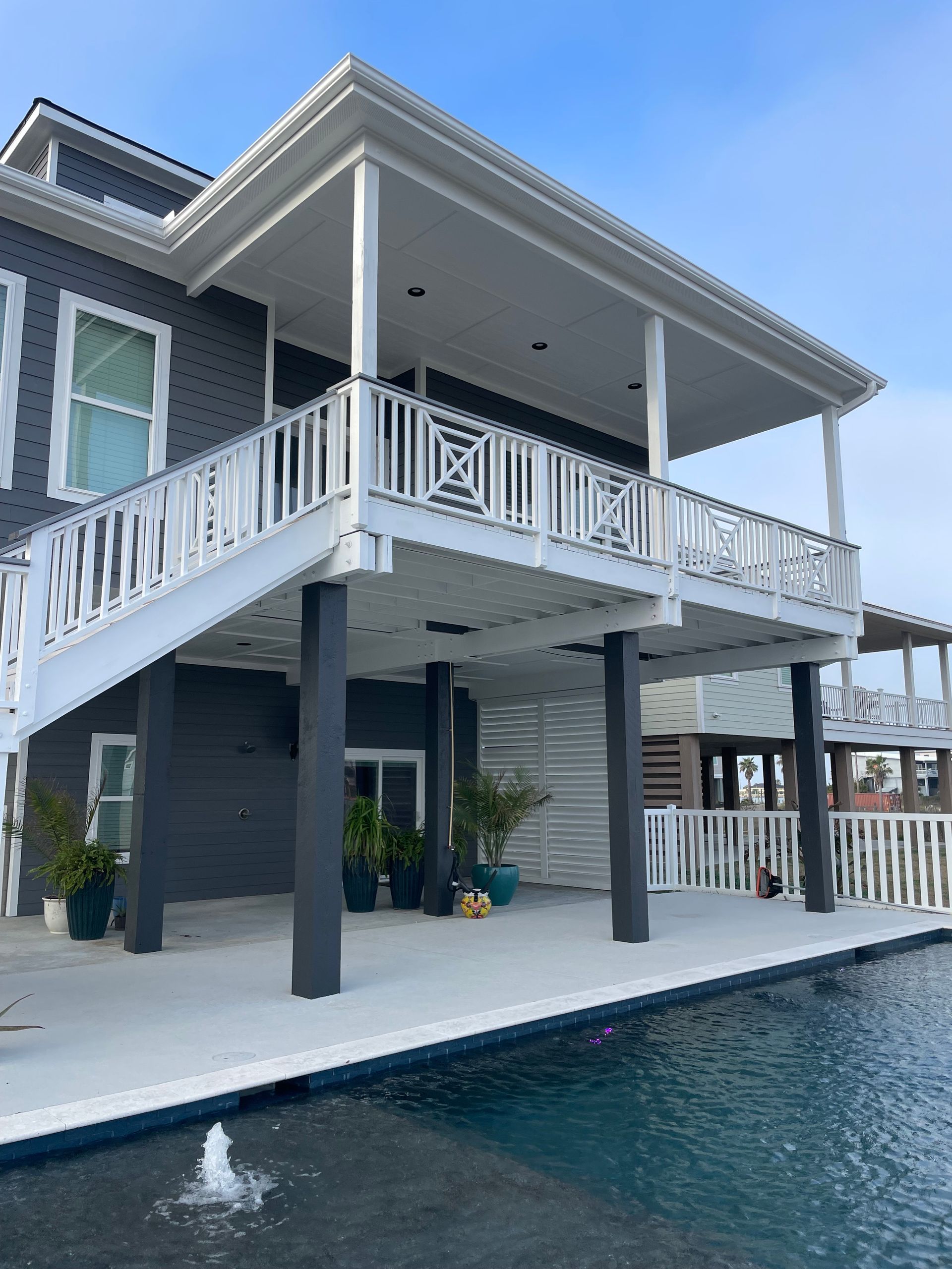 A gray house with a white deck overlooking a pool. White railings and support columns are visible.