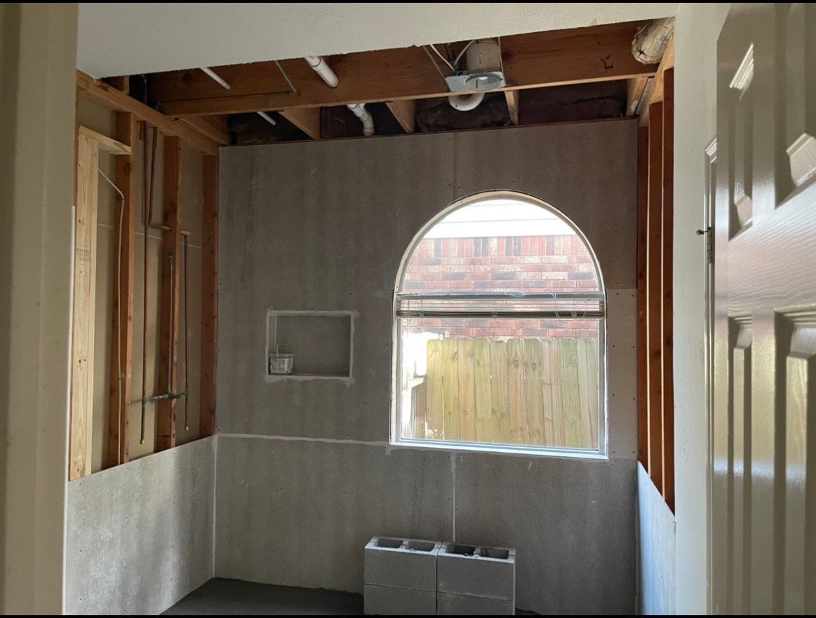 Bathroom renovation in progress: Framing exposed, cement backerboard installed, arched window. Concrete block on floor.