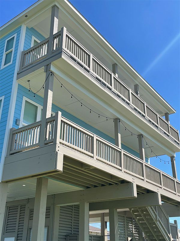 Person beside a white house with outdoor staircase and several black trash bags and buckets of paint on a green lawn.