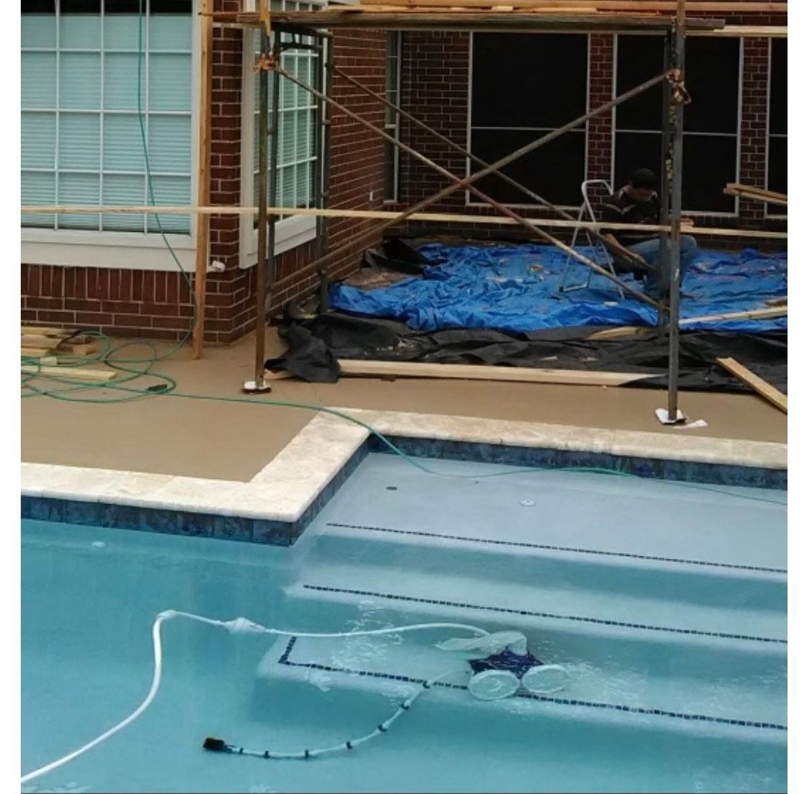 A pool cleaner robot in a swimming pool with steps; a house under construction is in the background.