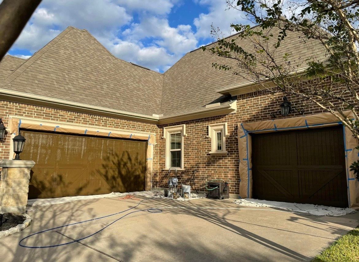 Brown garage doors on a stone house, driveways covered with white protection, blue tape outlining the door frames.