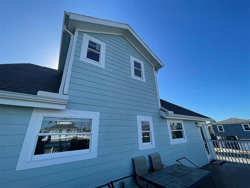 Person beside a white house with outdoor staircase and several black trash bags and buckets of paint on a green lawn.