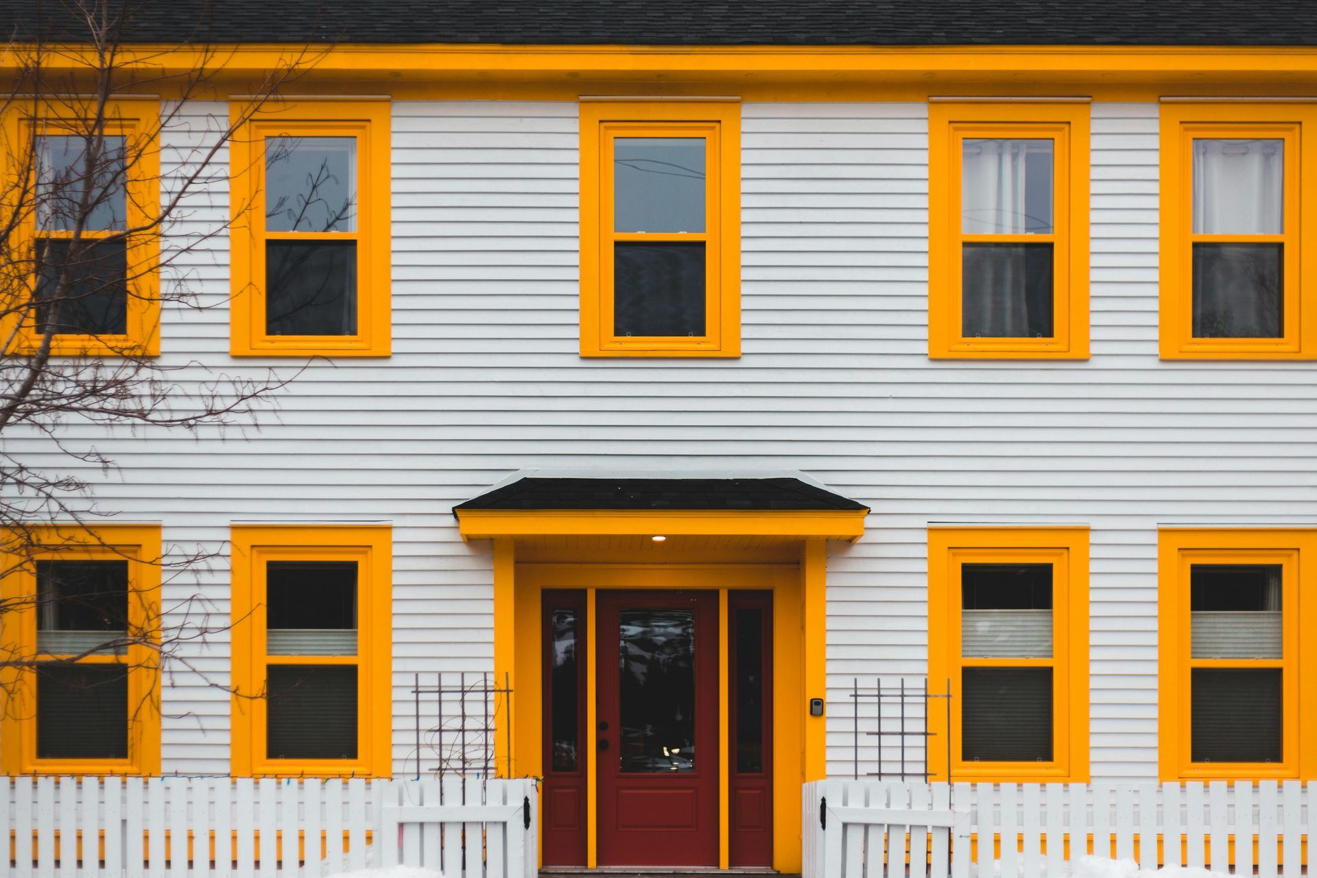 A two-story house with white horizontal siding, bright yellow window frames, and a dark red front door.