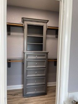 Gray built-in closet cabinet with drawers and shelves in a small room with closet rods.
