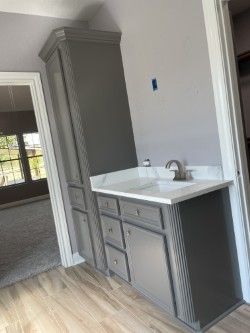 Gray bathroom cabinet with countertop sink and tall storage unit, set against a light gray wall.