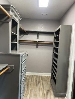 A grey-painted walk-in closet with built-in shelves, drawers, and hanging rods. The floor is wood-look laminate.