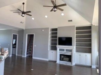 Living room with a fireplace, built-in shelves, and a TV. It has wood floors, gray walls, a vaulted ceiling, and two ceiling fans.