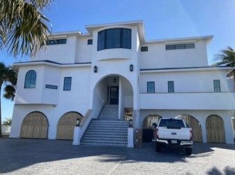 White stucco house with arched garage doors, a gray driveway, and a blue sky; a truck is parked in front.