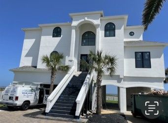 White two-story house with black accents and stairs leading to the front door; parked van with logo in front.