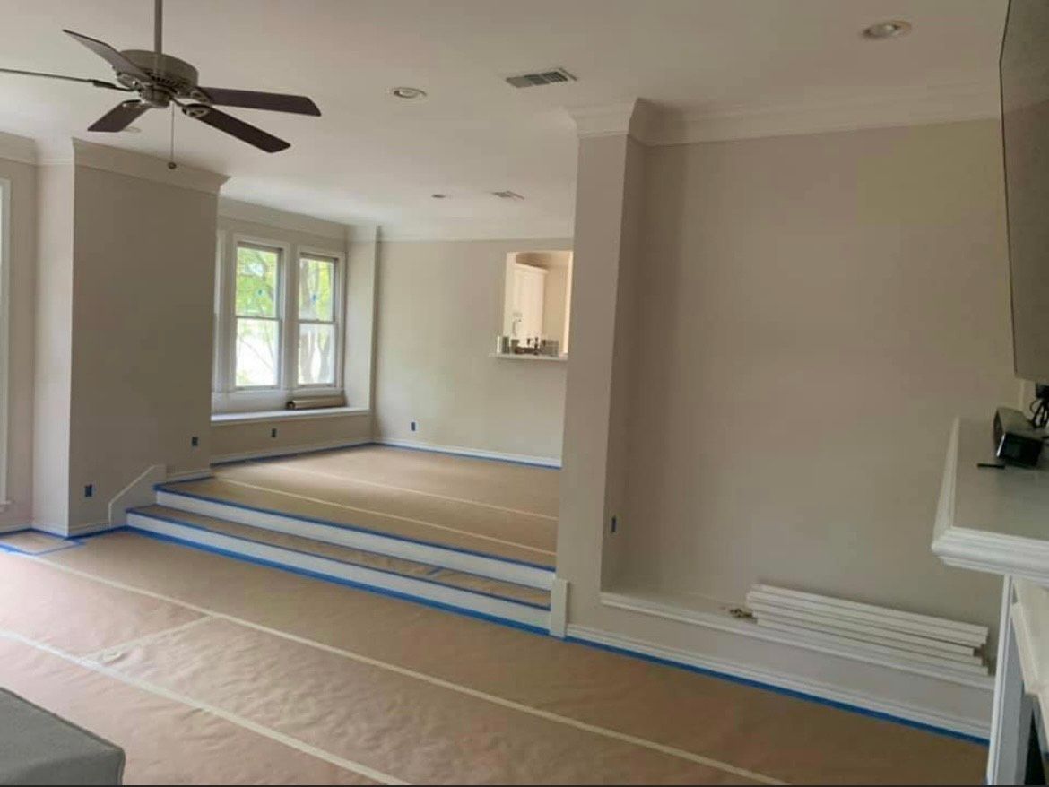 A newly painted interior with a raised floor section, a window, and a ceiling fan. Brown paper covers the floors.