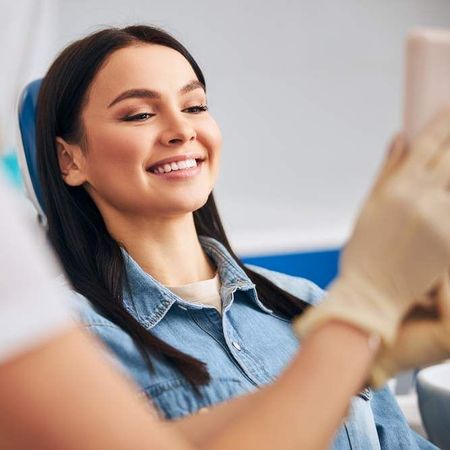 Woman smiles while looking in a dental mirror in a dentist’s chair.