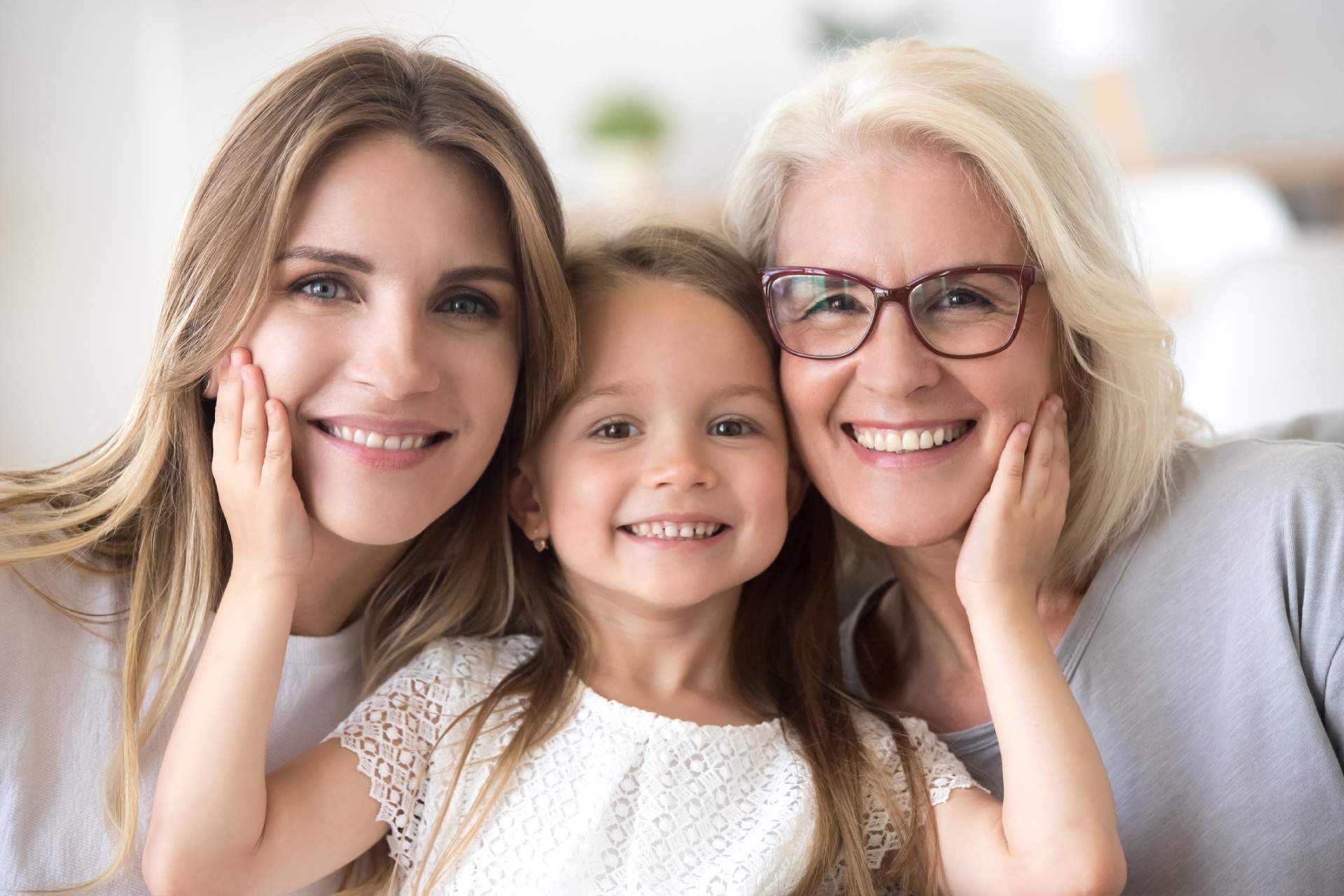 Woman, child, and older woman smiling, touching their faces.