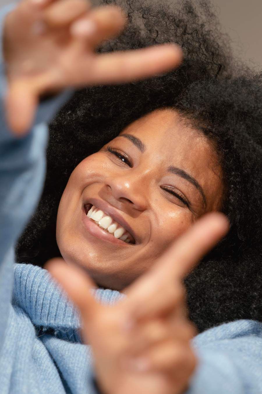 Woman smiling, making a frame with her hands. Light blue sweater.