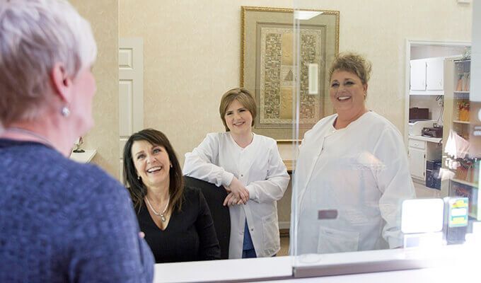 Patient at desk greets three smiling employees at a medical office.