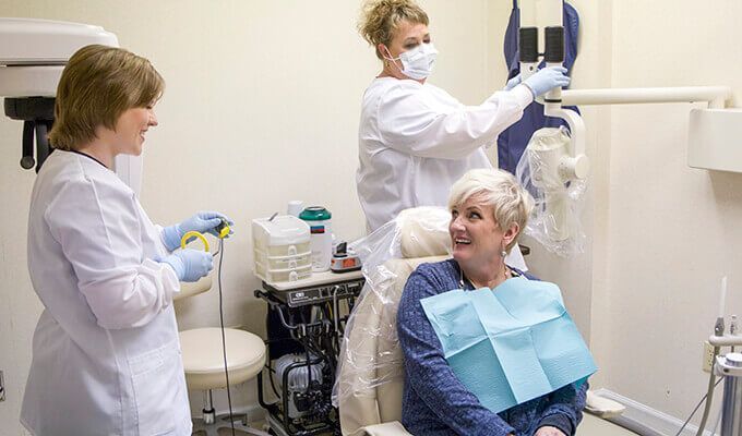 Woman in dental chair, two dental hygienists preparing for a procedure.