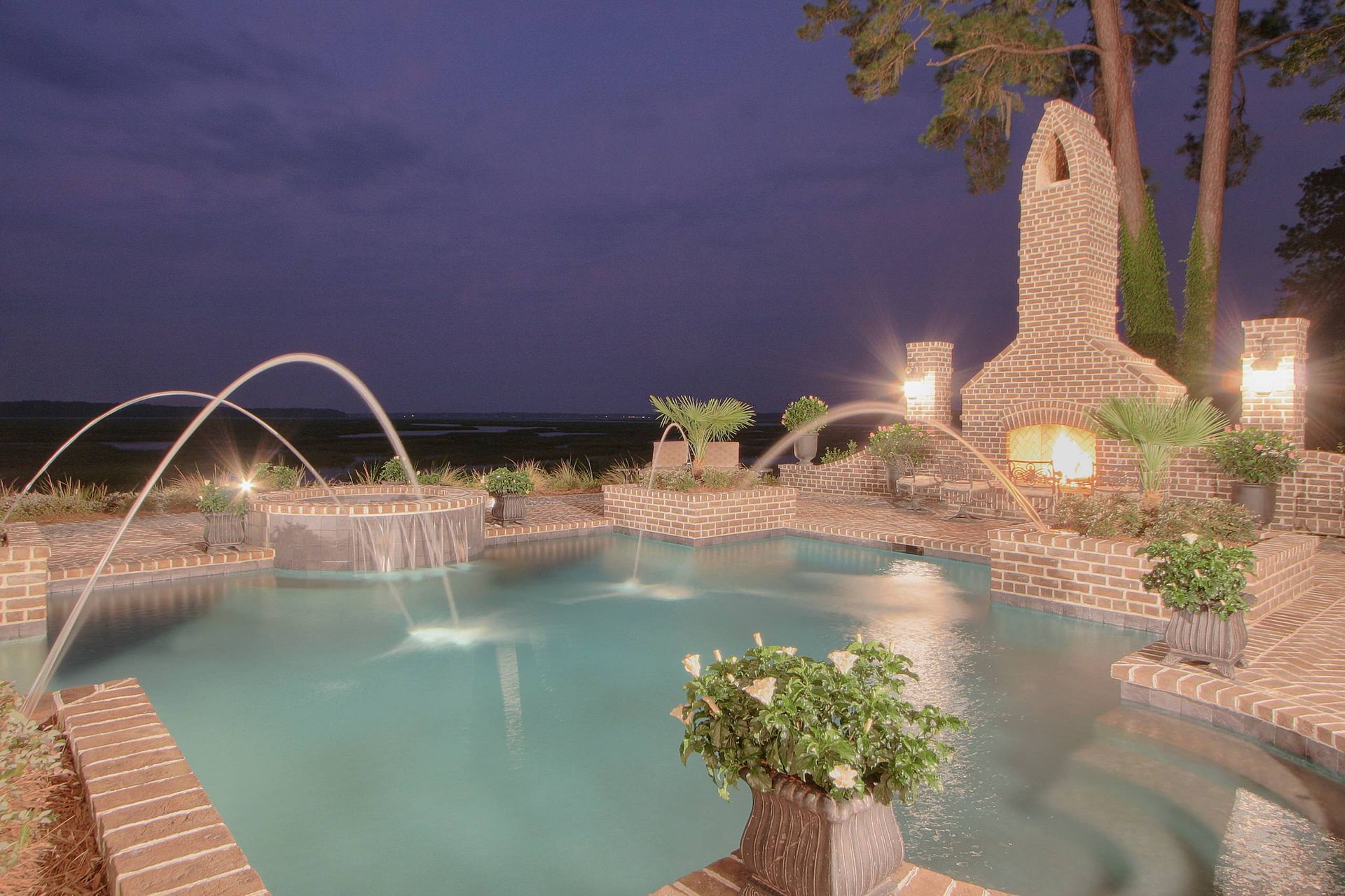 A large swimming pool with a fountain in the middle at night