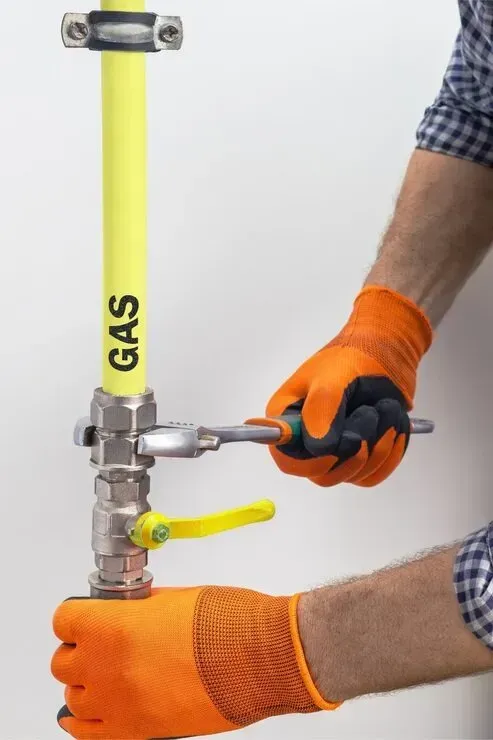 Gloved worker tightening a gas valve on a yellow gas pipe with a wrench