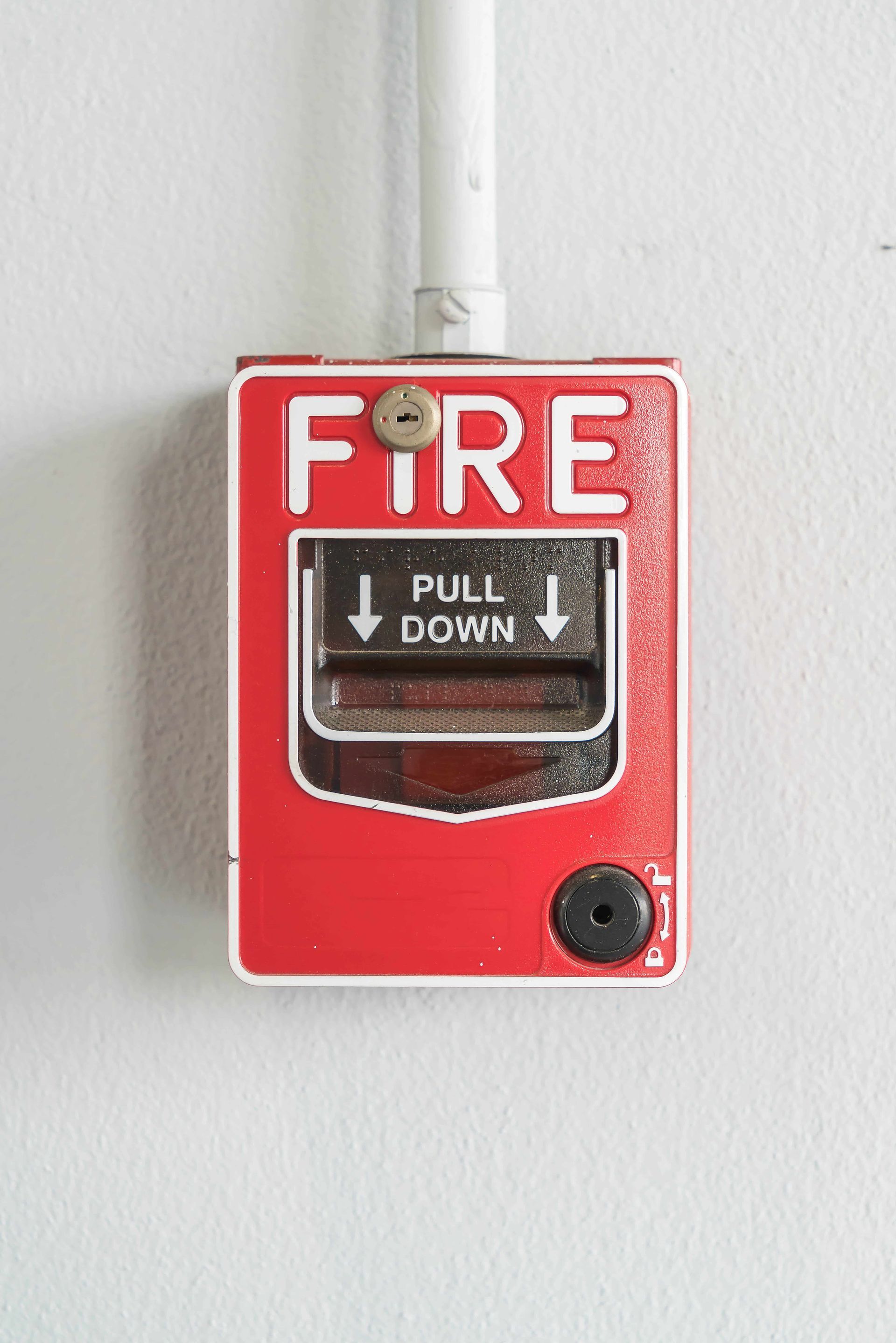 A red fire alarm is hanging on a white wall.