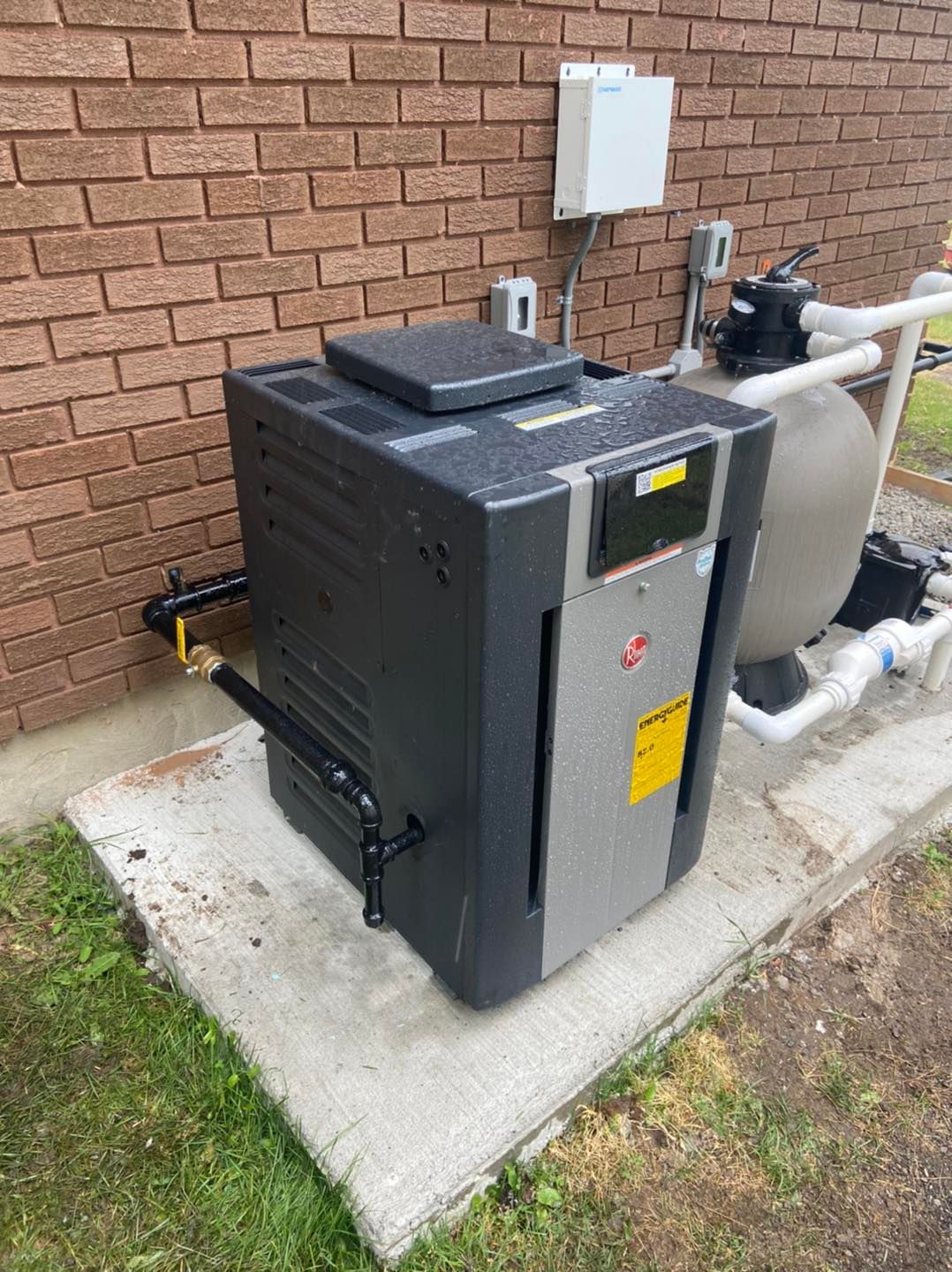 A swimming pool heater is sitting on the side of a brick building.