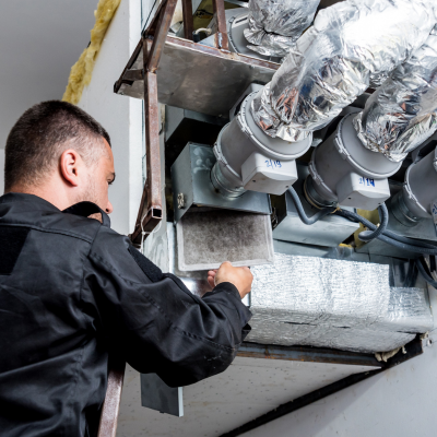 A man is standing on a ladder working on a ventilation system.