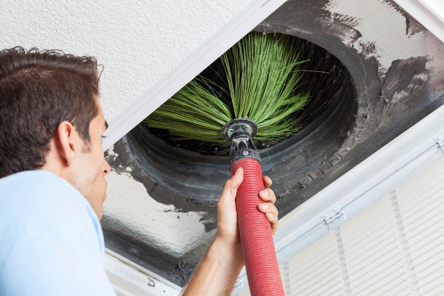 Man using a brush to clean an air duct