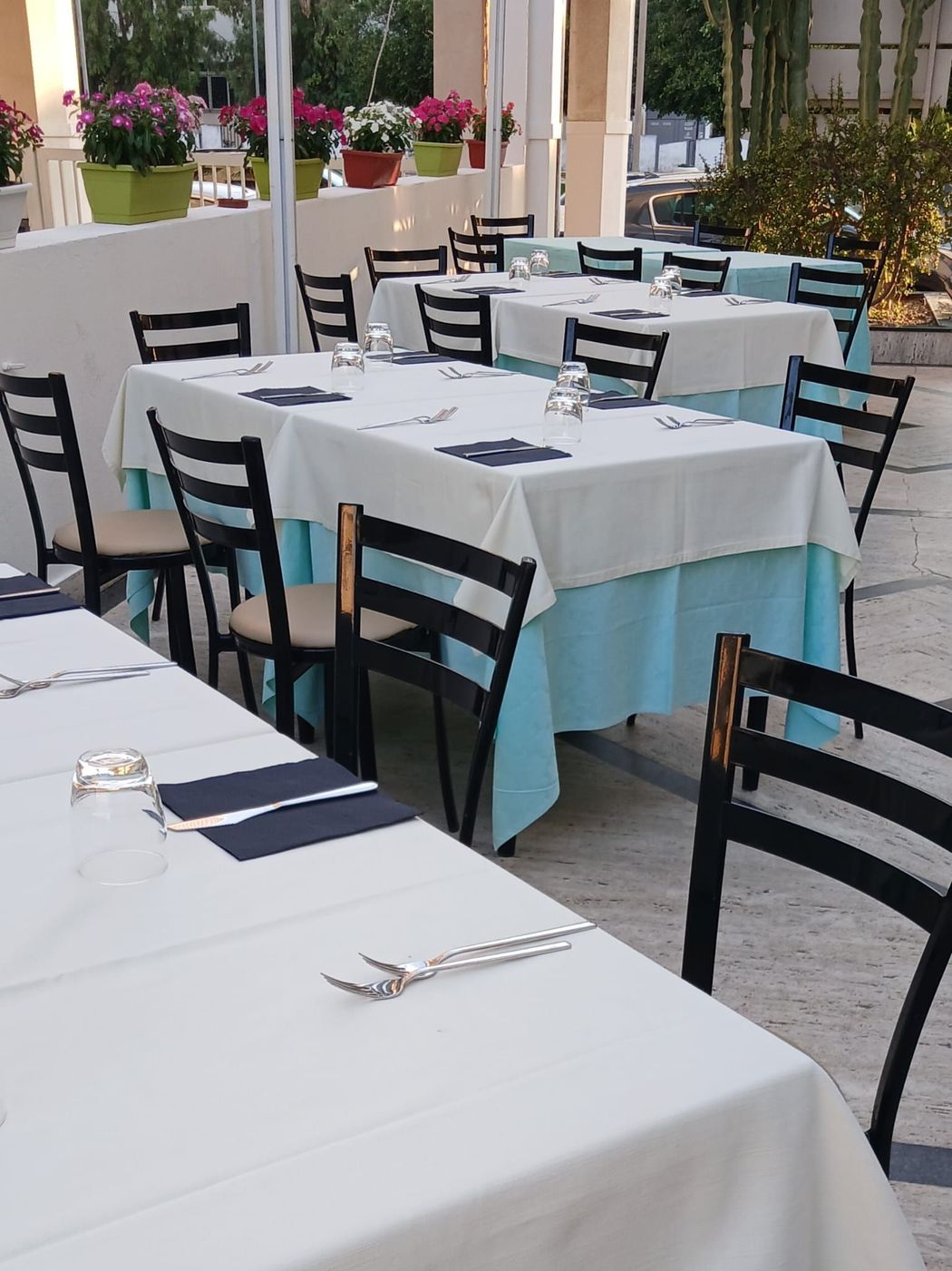 Tavoli da ristorante all'aperto apparecchiati con tovaglie bianche e dettagli blu su un patio