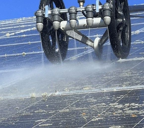 Ein Reinigungsroboter sprüht Wasser auf ein Solarpanel und entfernt so Schmutz und Ablagerungen.