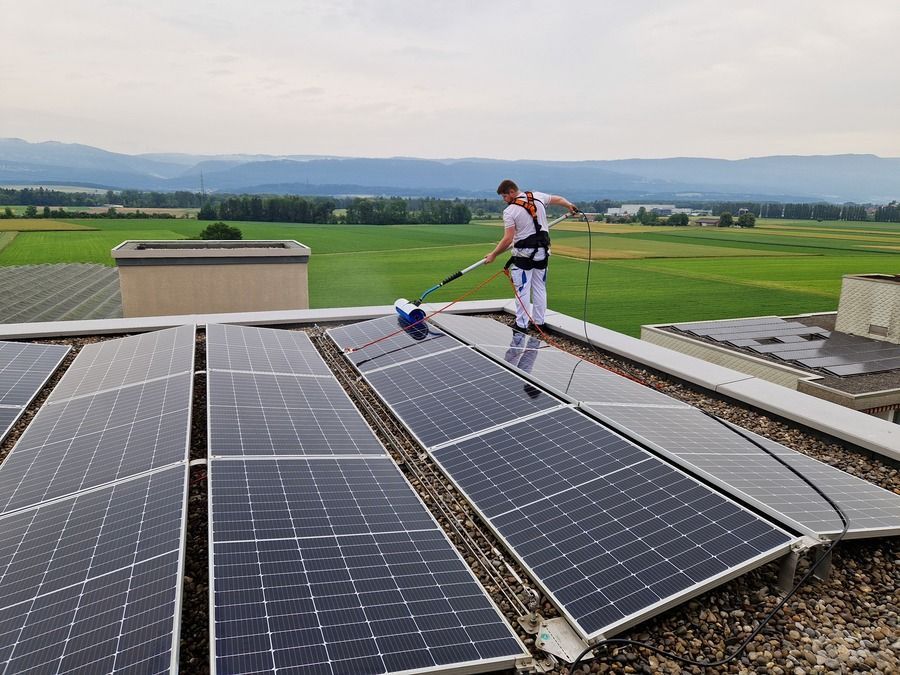 Ein Mann reinigt Solarmodule auf dem Dach eines Gebäudes.