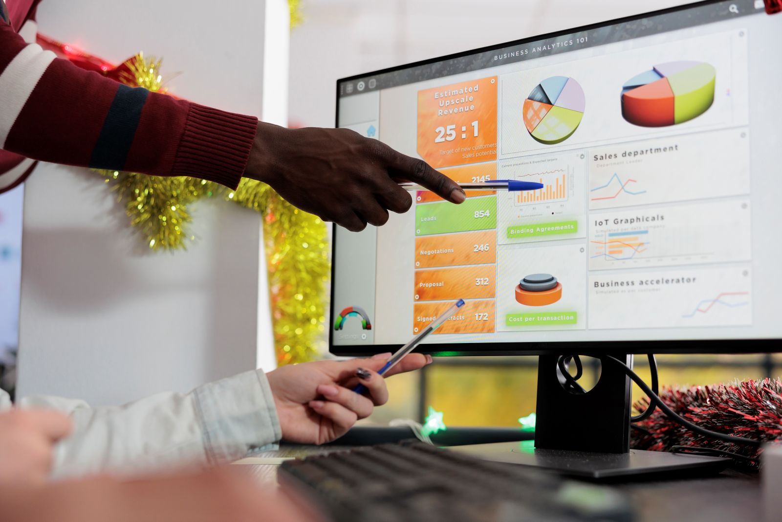 Two people pointing at a computer screen displaying charts and graphs, discussing data analysis.