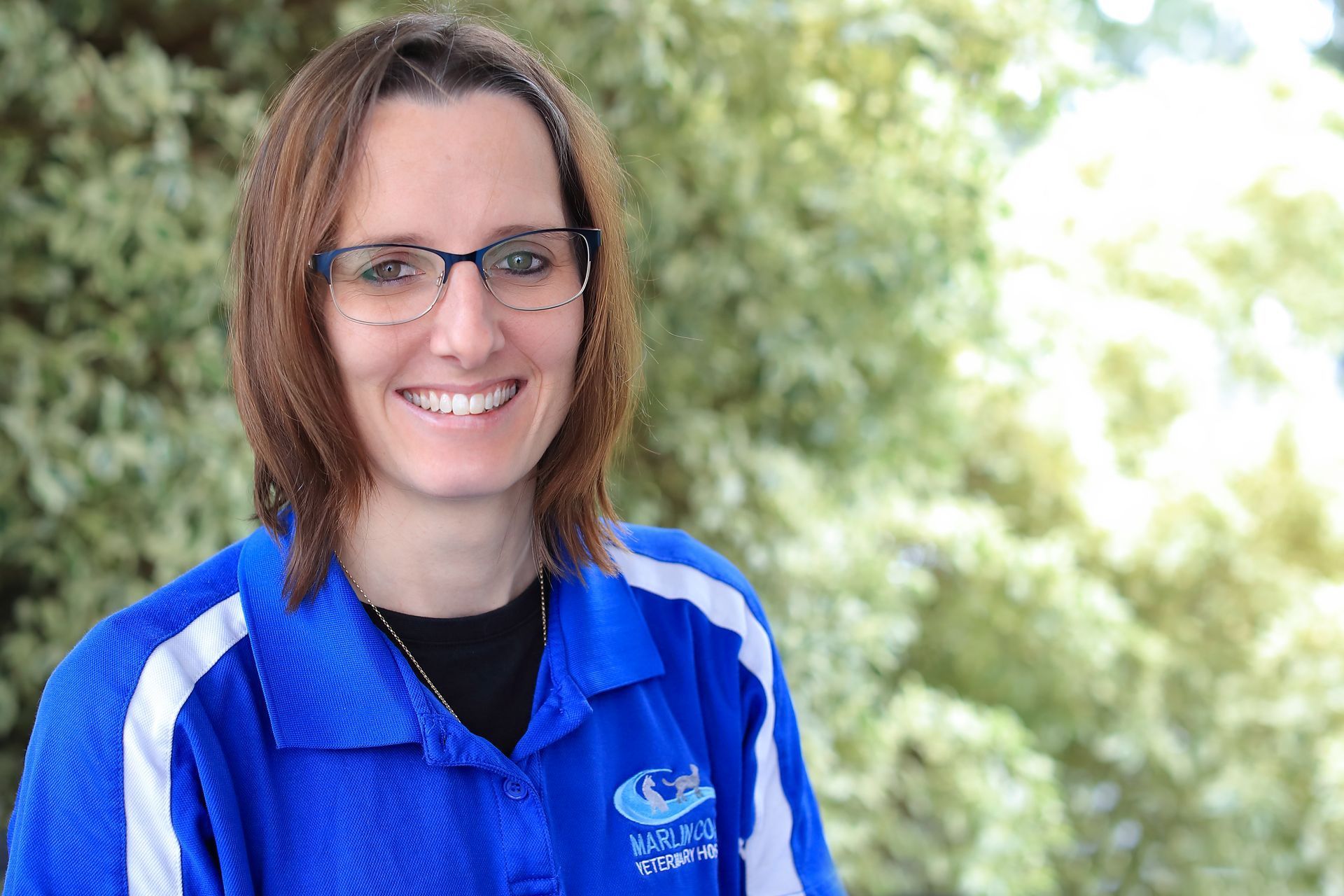 A woman wearing glasses and a blue shirt is smiling for the camera.