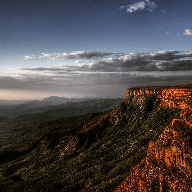 Capture the breathtaking vista of Angola's Tundavala Gap, a majestic canyon glowing under the soft light of sunset. The towering cliffs are brilliantly painted in orange reflections, contrasting against the deep dark blue and grayish sky above. This stunning view of Angola's untouched wilderness, clear except for some flat clouds, offers a truly unique experience. Inspiration Africa specializes in organizing tailor-made travel and expedition-style journeys to explore Angola's hidden highlights, including this spectacular natural wonder. Discover the wild beauty of Angola travel with us