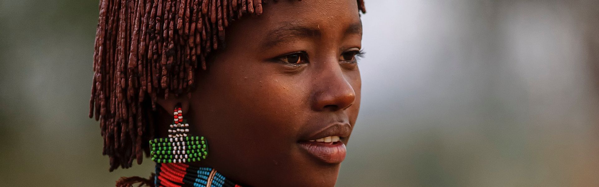 Capture the rich cultural heritage of the Omo Valley with this striking photo of a Hamer Tribe woman in Ethiopia. She is adorned in full traditional attire and makeup, showcasing the distinct style of the Hamer people, and looks thoughtfully into the distance. Inspiration Africa specializes in designing your unique, tailor-made trip to Ethiopia for respectful cultural immersion and exploring other incredible destinations across Africa. Experience authentic African traditions with us!