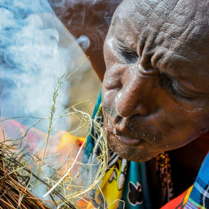 Witness the traditional survival skills of the Maasai in Kenya with this powerful close-up photo. A Maasai man concentrates intensely, blowing carefully into a piece of hay to coax a small fire flame and smoke, demonstrating the ancient art of fire-starting. Inspiration Africa specializes in designing your unique, tailor-made trip to Kenya for authentic cultural immersion and exploring other spectacular destinations across Africa. Experience the traditions of the Maasai warriors with us!