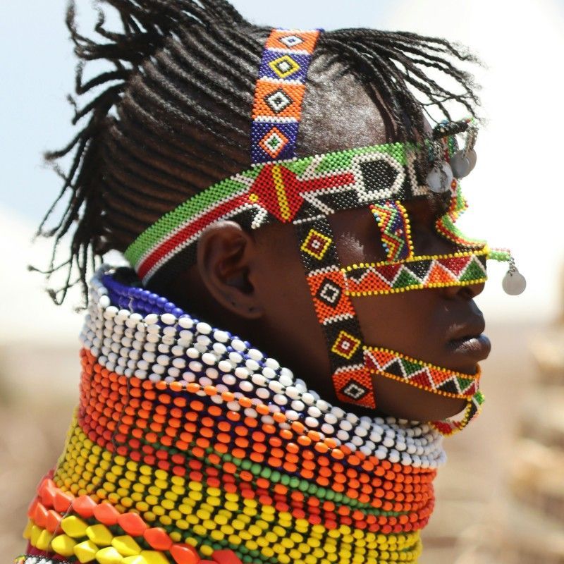 Focus on the detail of Turkana Tribe tradition in this close-up photo from Kenya. The image clearly shows the man's head as a woman's hands meticulously adjust or secure his traditional attire. This moment emphasizes the intricate craftsmanship and respectful process involved in their cultural dress. Inspiration Africa specializes in designing your unique, tailor-made trip to Kenya for engaging cultural immersion and exploring other spectacular destinations across Africa. Experience authentic Kenyan customs with us!