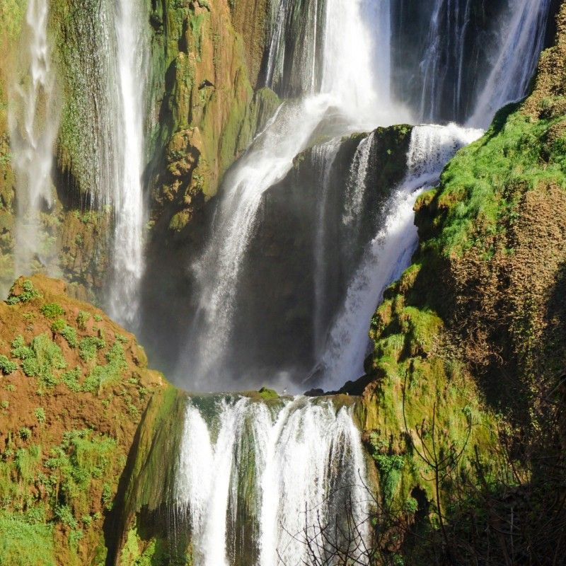 Discover the stunning Ouzoud Falls, the second highest waterfalls in Africa, captured here in a dramatic front-on view. Witness the cascades where four smaller waterfalls merge into one powerful torrent, set against the striking earthy reddish-brown landscape typical of the Moroccan Atlas Mountains. The hint of green foliage adds contrast to this magnificent scene. Inspiration Africa specializes in organizing tailor-made travel to Morocco's hidden gems, including this breathtaking site. Let us craft your perfect journey to explore the culture and natural beauty of the Atlas region and beyond