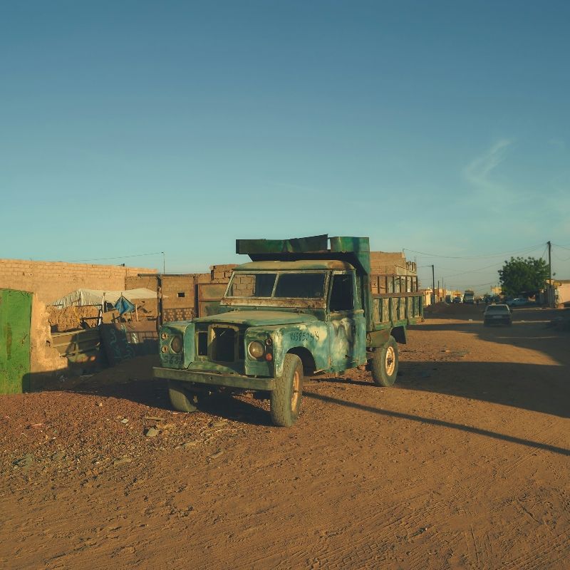 This evocative image shows a dust-covered truck parked along a sandy street in a desert town in Mauritania, capturing the rugged charm and timeless rhythm of life on the edge of the Sahara. Surrounded by arid landscapes and golden dunes, towns like Chinguetti, Atar, and Ouadane offer a glimpse into Mauritania’s unique culture, history, and resilience. Inspiration Africa designs tailor-made journeys to Mauritania, taking travelers off the beaten path to explore desert settlements, ancient trading posts, and nomadic traditions. Experience the raw beauty and remote allure of Mauritania with expertly curated travel from Inspiration Africa.