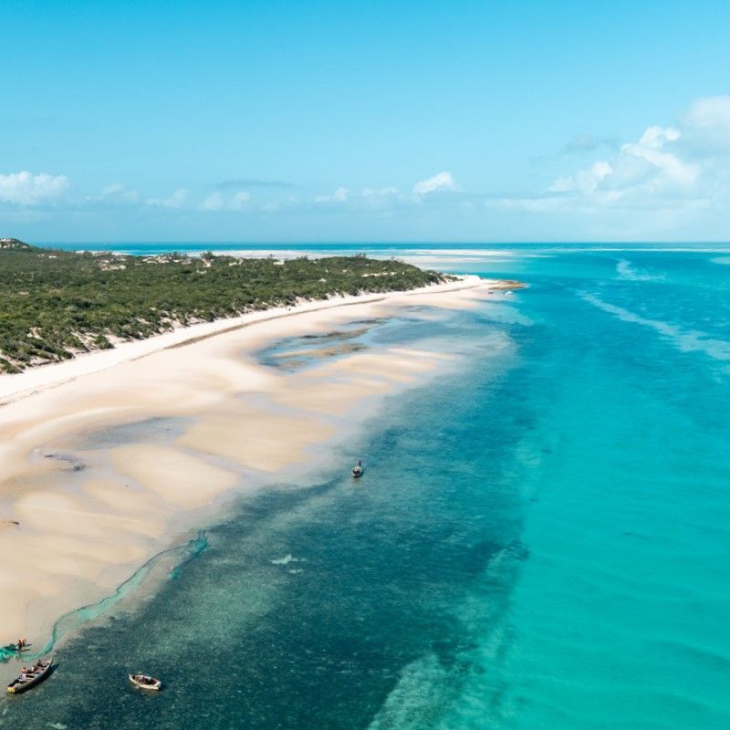 Discover the secluded paradise of Benguerra Island in Mozambique's Bazaruto Archipelago. This magnificent aerial photo reveals a perfect curve of dazzling white sand beach meeting the bright turquoise water. Lush, lovely green vegetation flanks the water's edge, highlighting the island's pristine nature. Inspiration Africa specializes in designing your exclusive, tailor-made trip to Benguerra and other extraordinary destinations across Africa. Book your dream beach holiday and dive adventure with us!